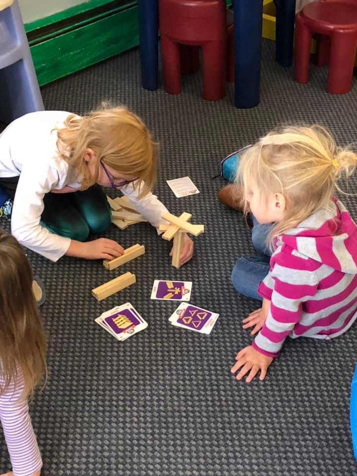 Two children playing with wooden blocks and cards on the floor