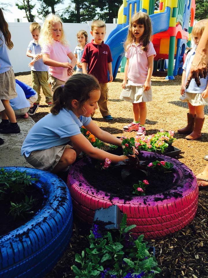 Child planting flowers in a tire planter with other children watching