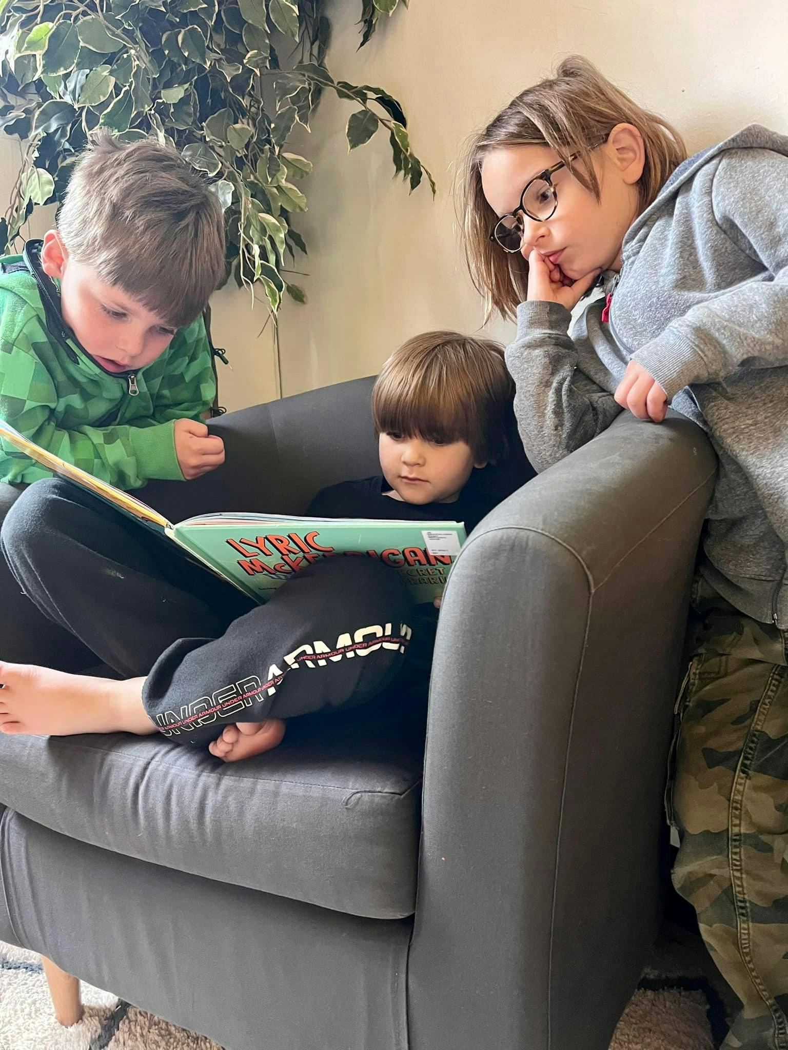 Three children reading a book together on a chair