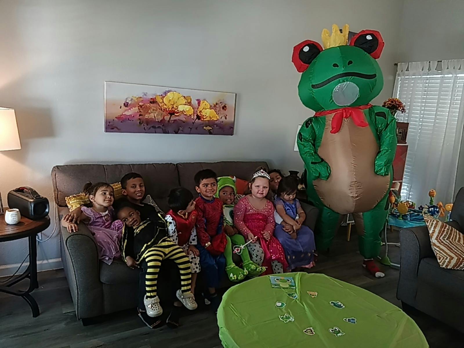 Children sitting on a couch with a large frog mascot standing next to them