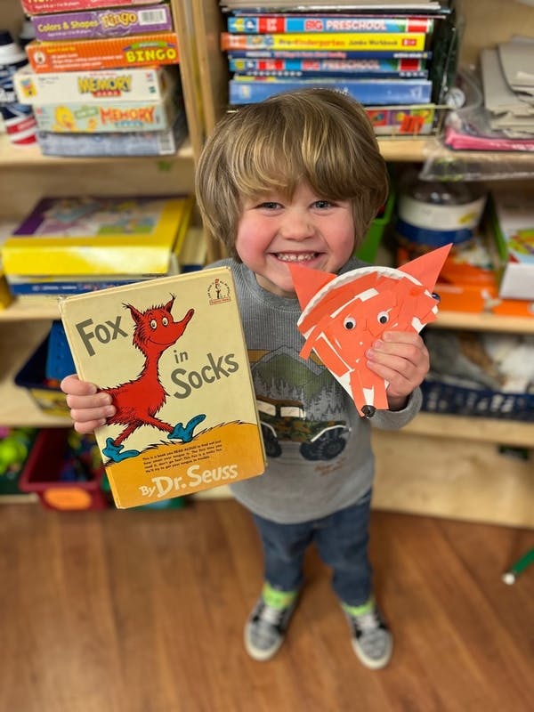 Child holding a "Fox in Socks" book and a paper fox craft