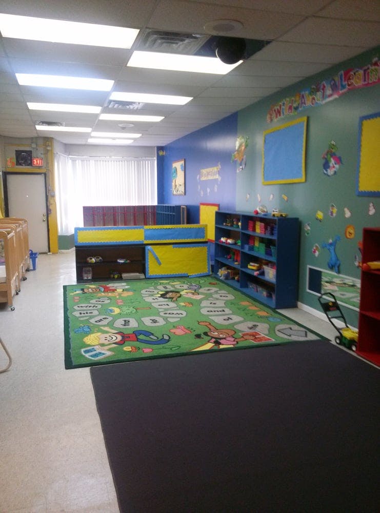 A colorful classroom with a play rug, shelves, and cribs