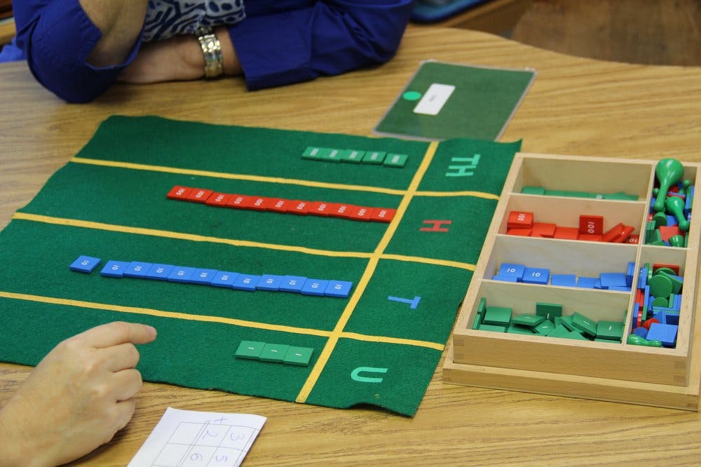 Person's hand pointing at a green mat with colorful blocks