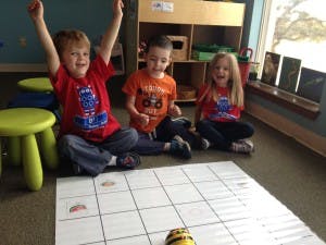 Three children playing with a robot on a grid