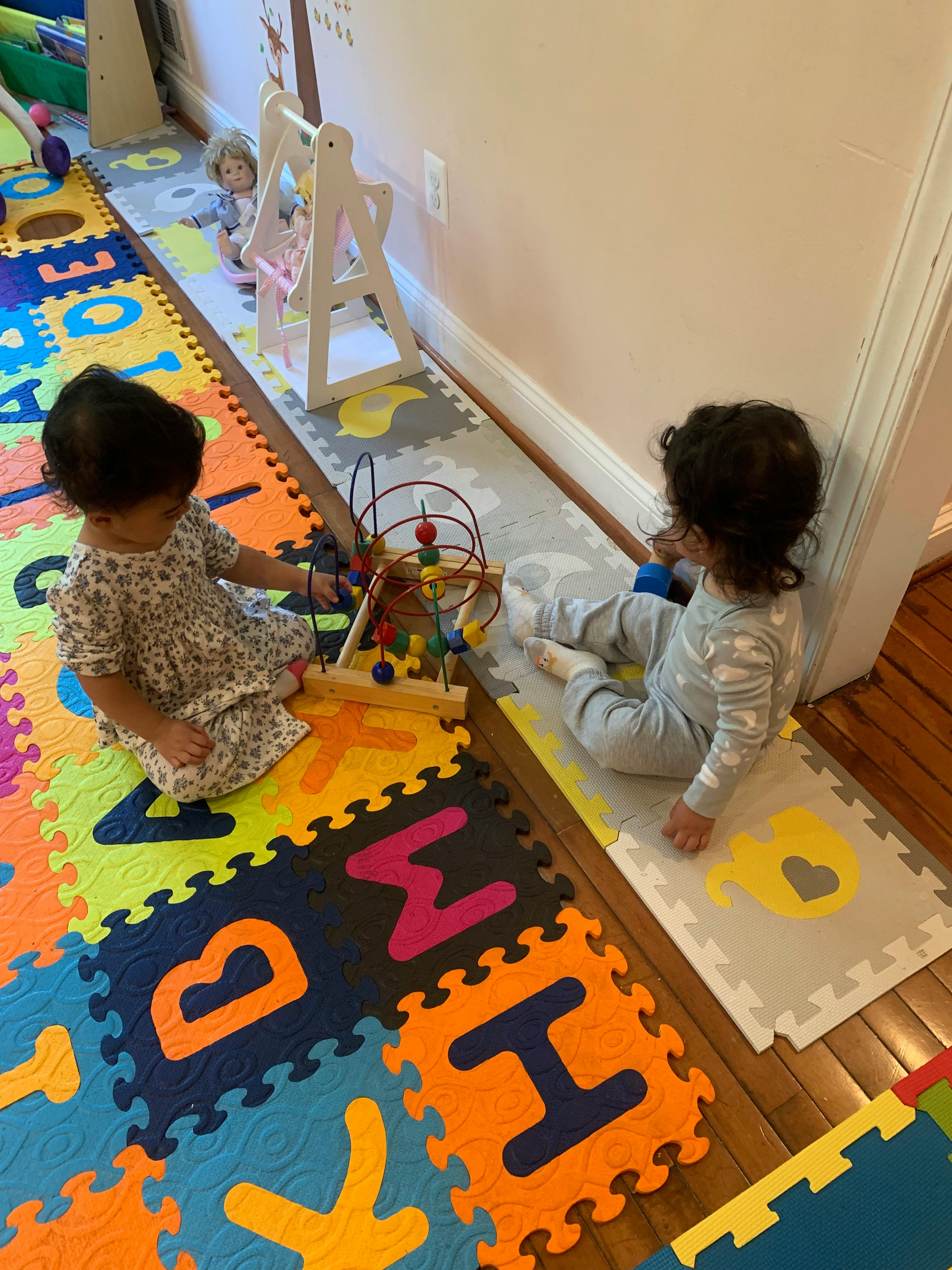 Two children playing on foam mats, one with a bead maze toy