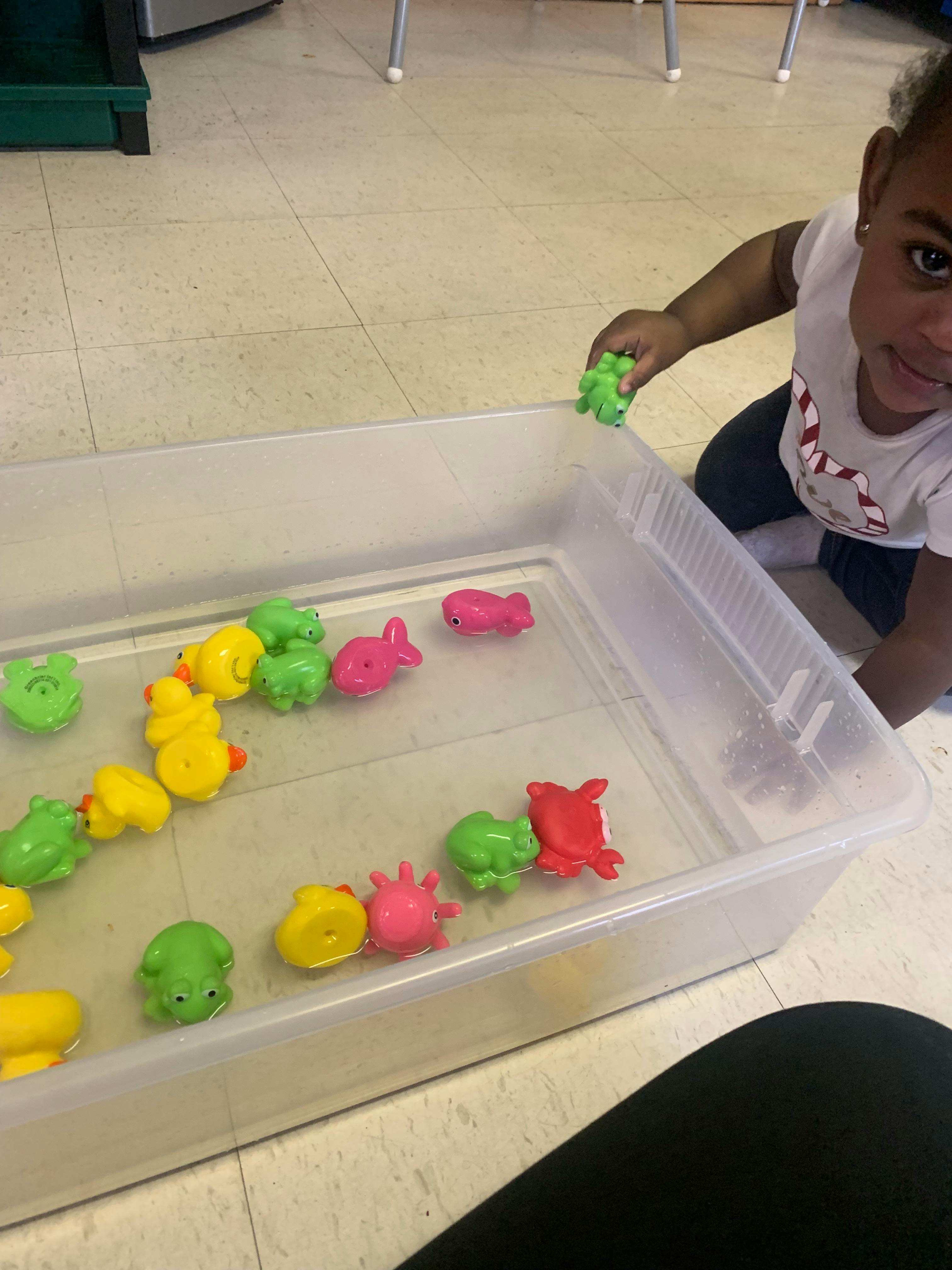 Child playing with colorful floating toys in a clear bin
