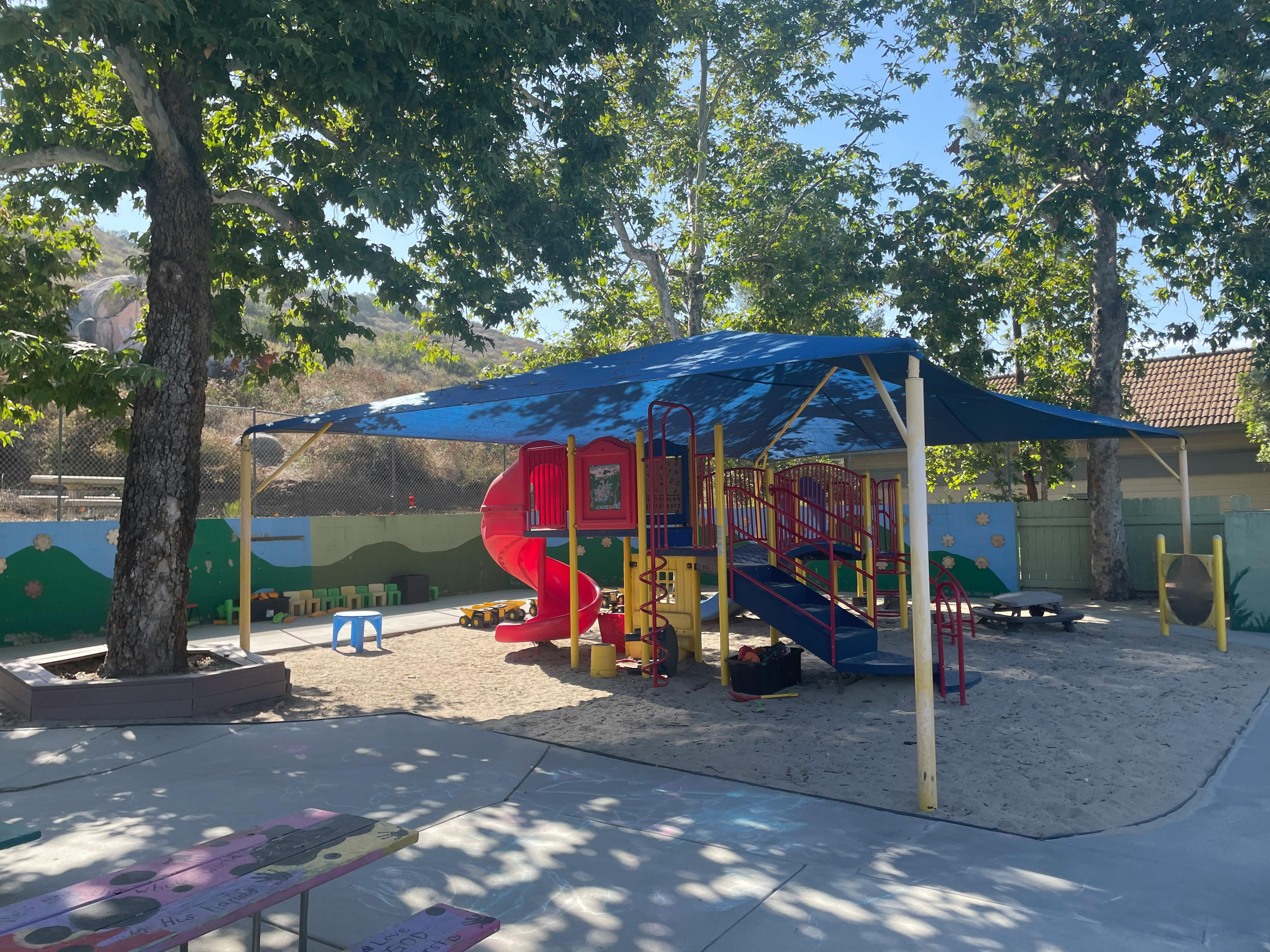 Playground with slides and climbing structures under a blue shade canopy