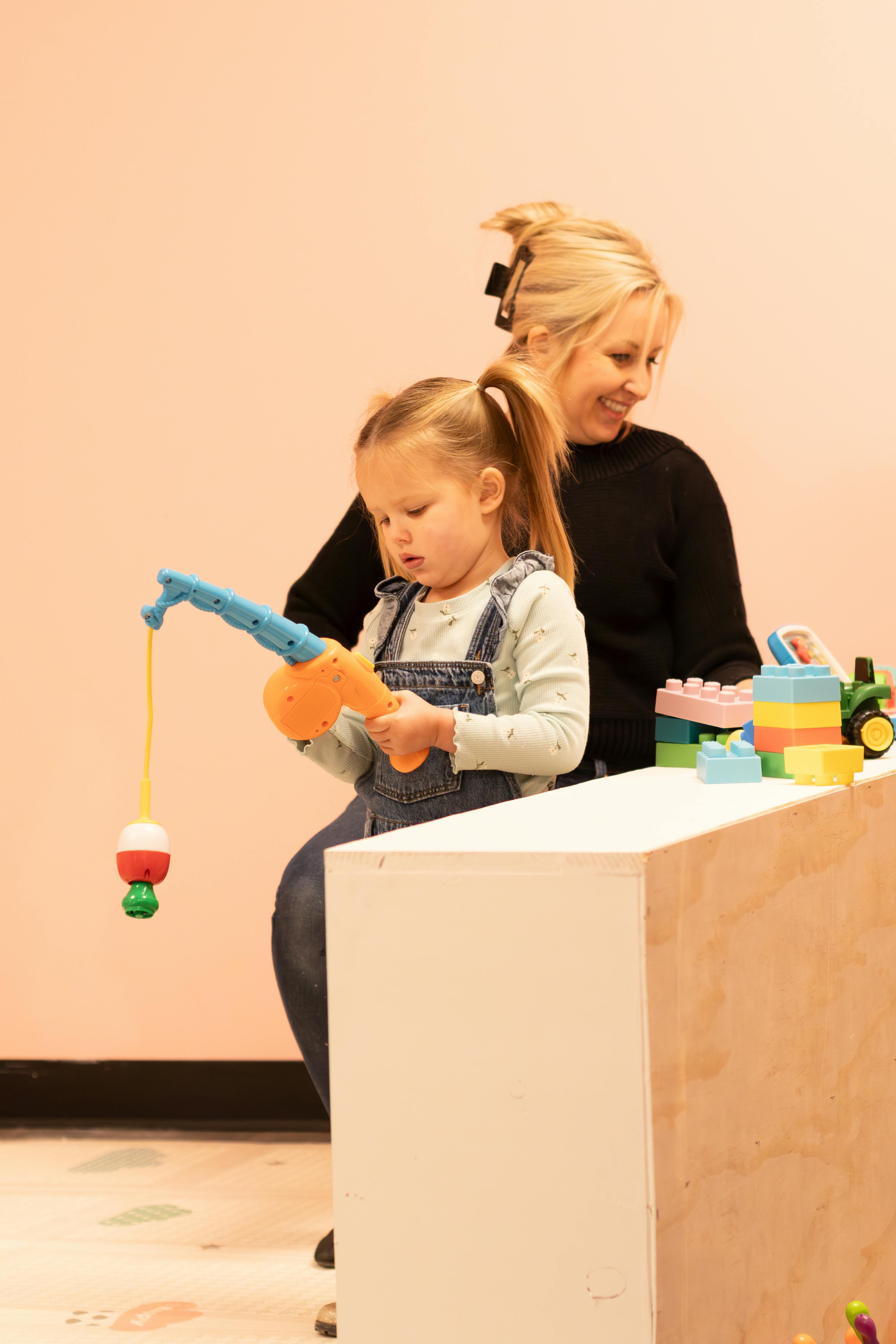Child playing with a toy fishing rod, person sitting behind