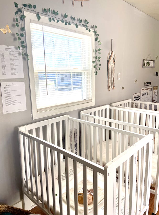 Multiple white cribs in a room with a window