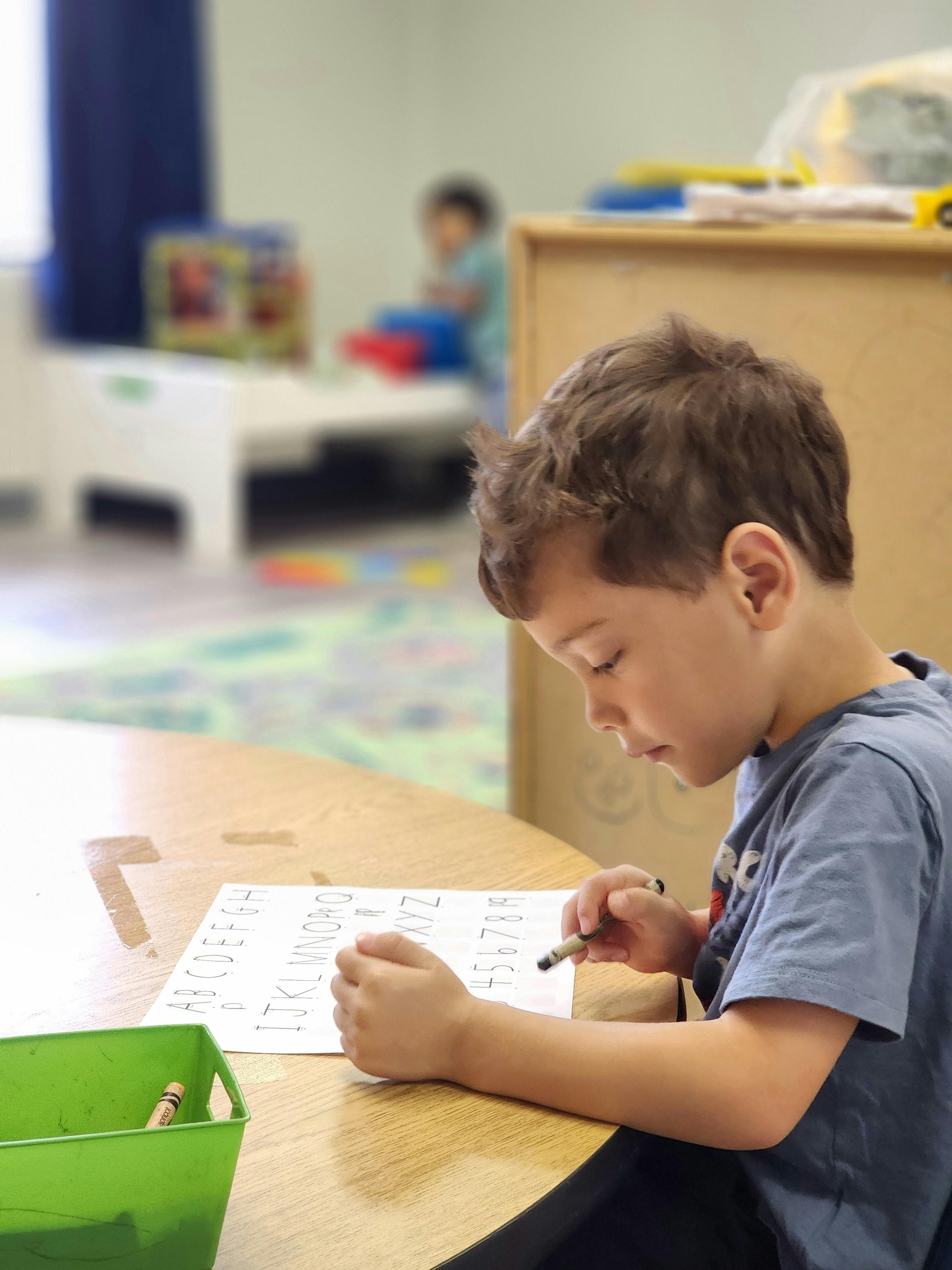 Child coloring a worksheet at a table in a classroom