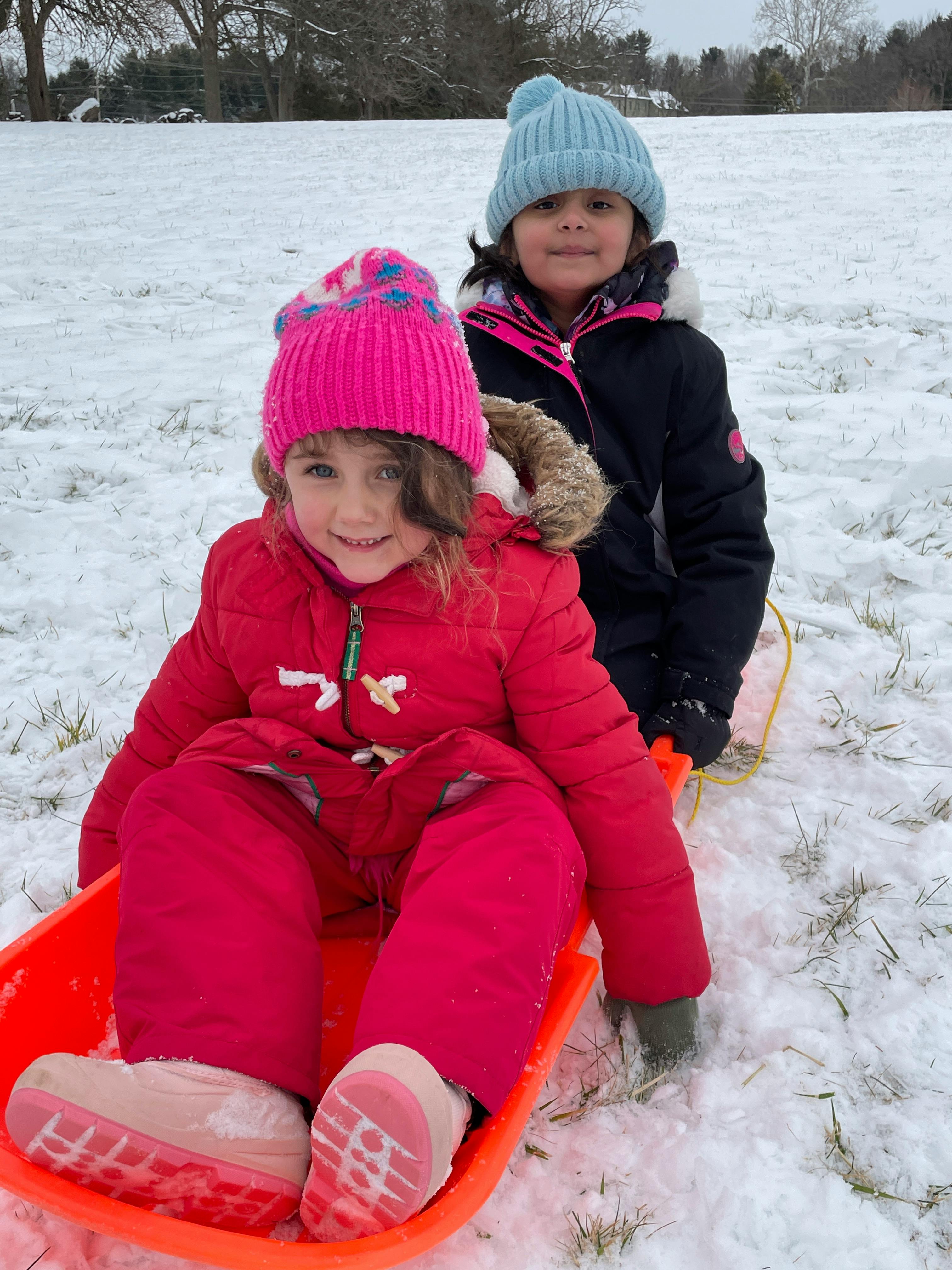 Two children in winter clothing on a sled in the snow