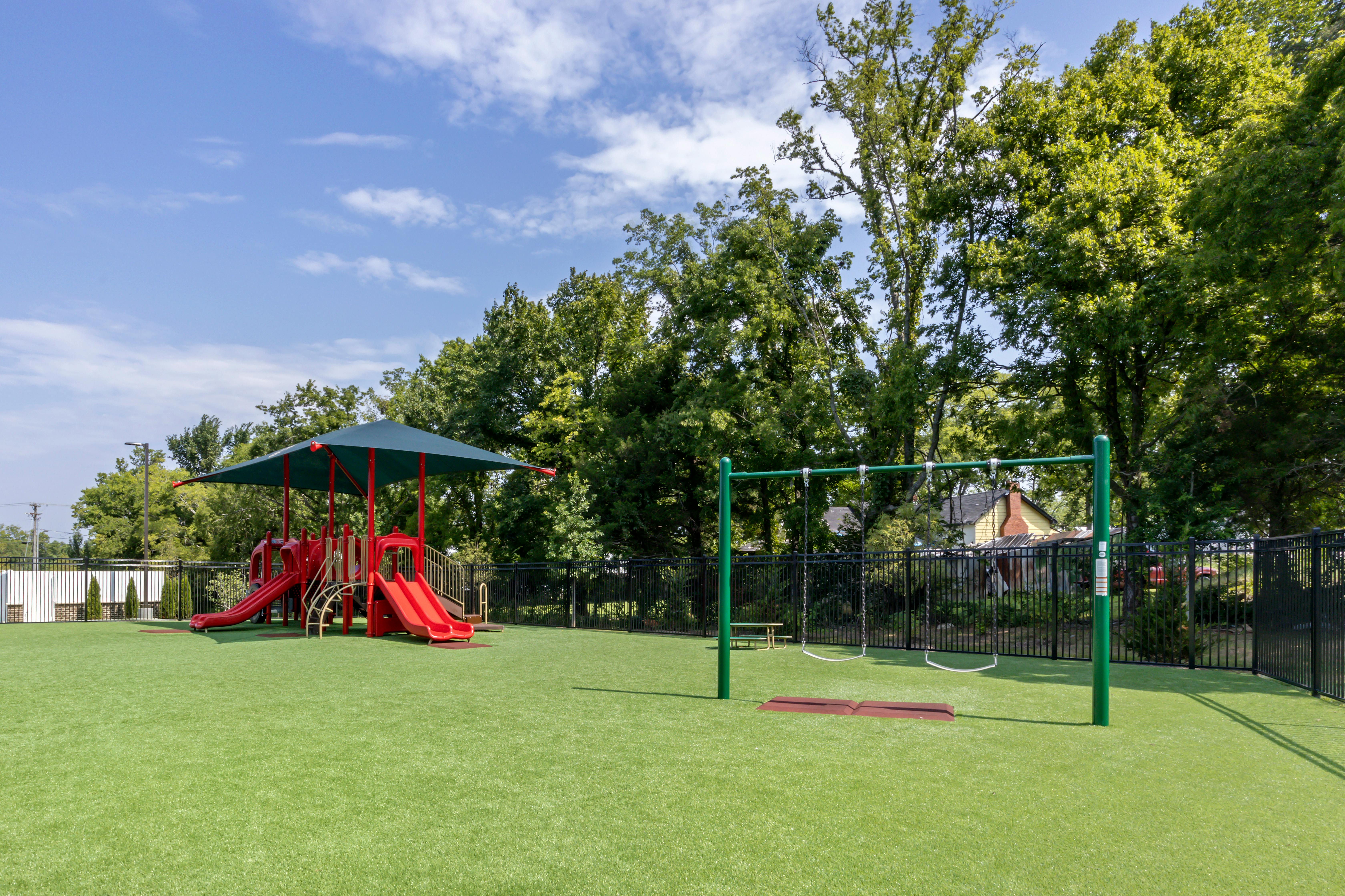 A playground with a red slide structure and swings on green artificial turf
