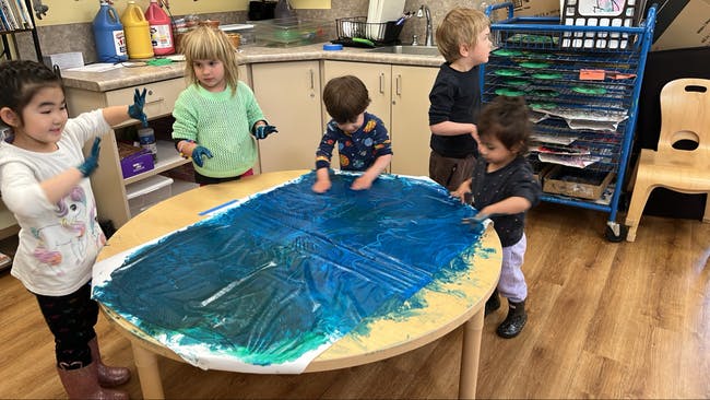 Children finger painting with blue paint on a table