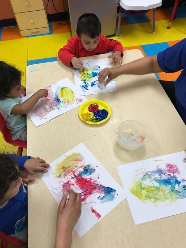 Children and an adult painting on paper at a table