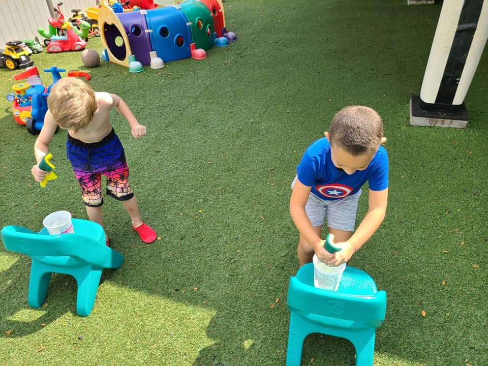 Two children playing with water and toys on green turf
