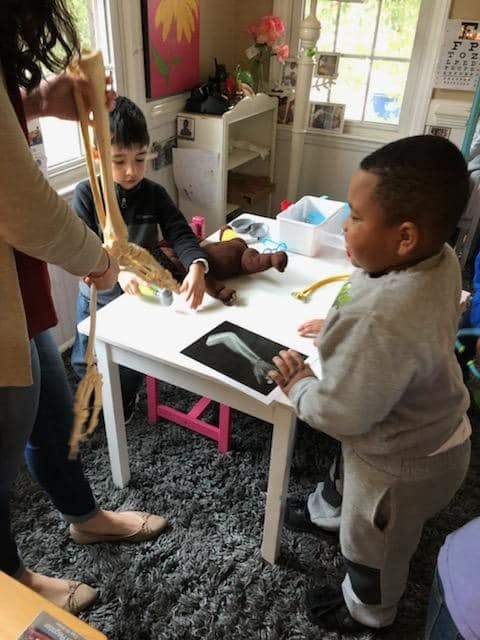 Person holding a skeleton model with two children at a table