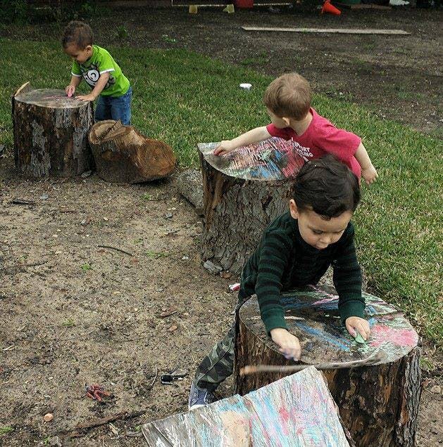 Three children drawing on tree stumps outdoors