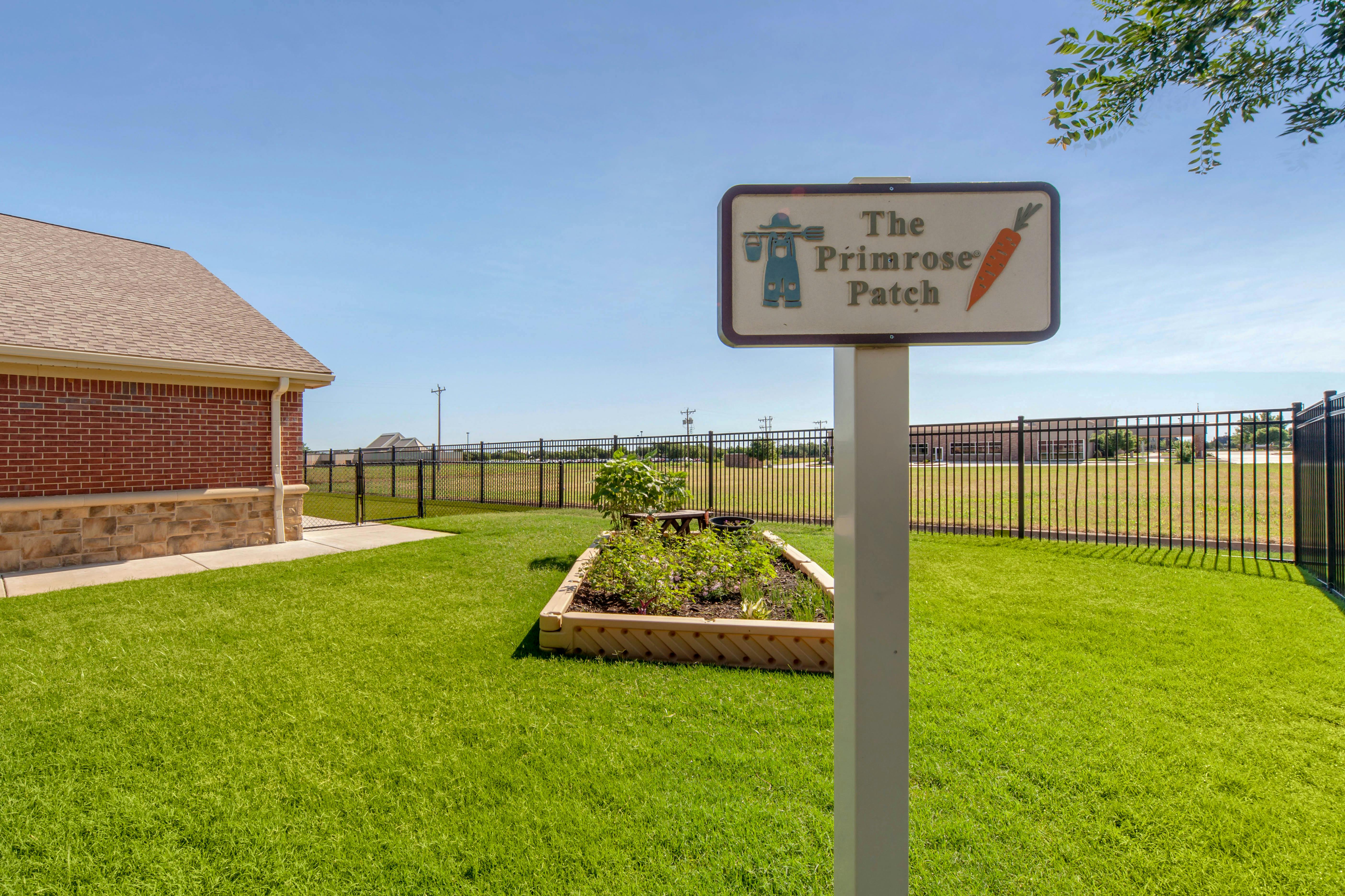 The Primrose Patch sign next to a garden bed and grassy area