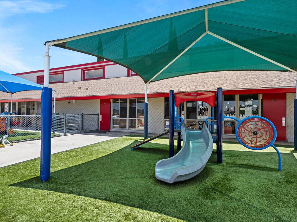 Playground area with artificial turf, a green slide, and red-roofed building