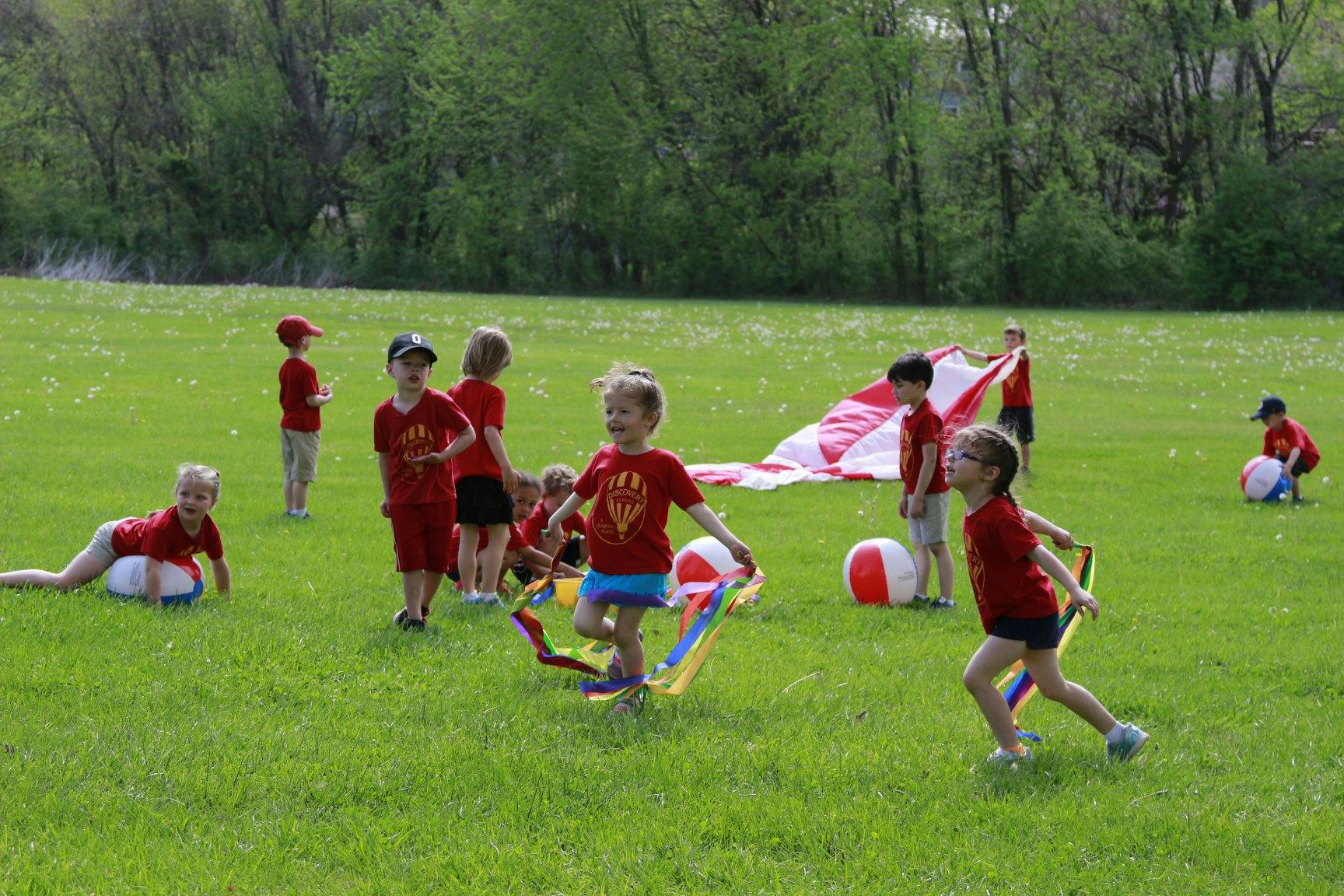 Children playing with a parachute and balls in a grassy field