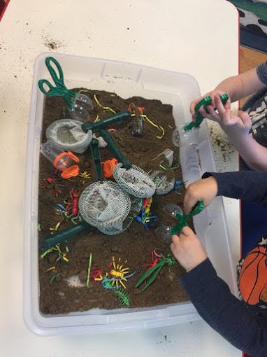Children playing with toy insects in a container of dirt