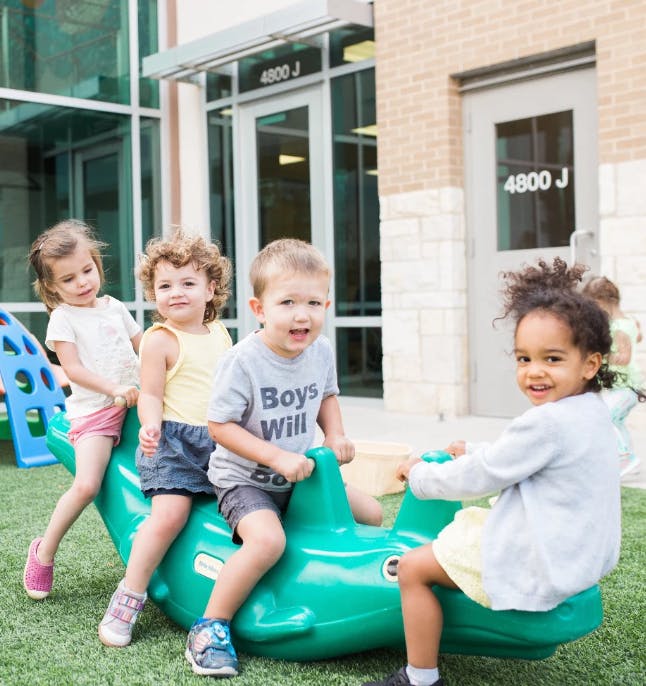 Four children playing on a green outdoor seesaw