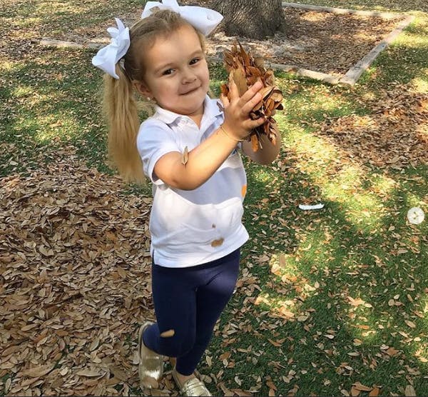Child holding a pile of leaves outdoors