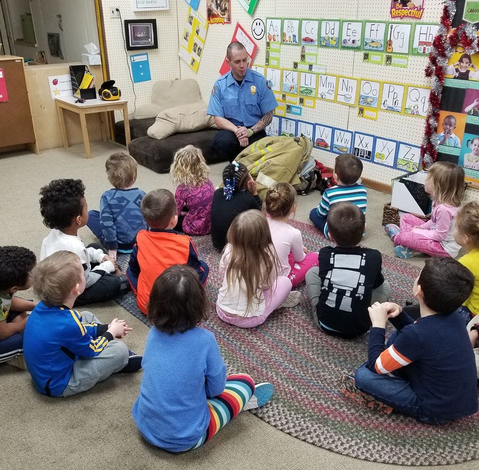 Adult in uniform sitting on floor with children in a classroom
