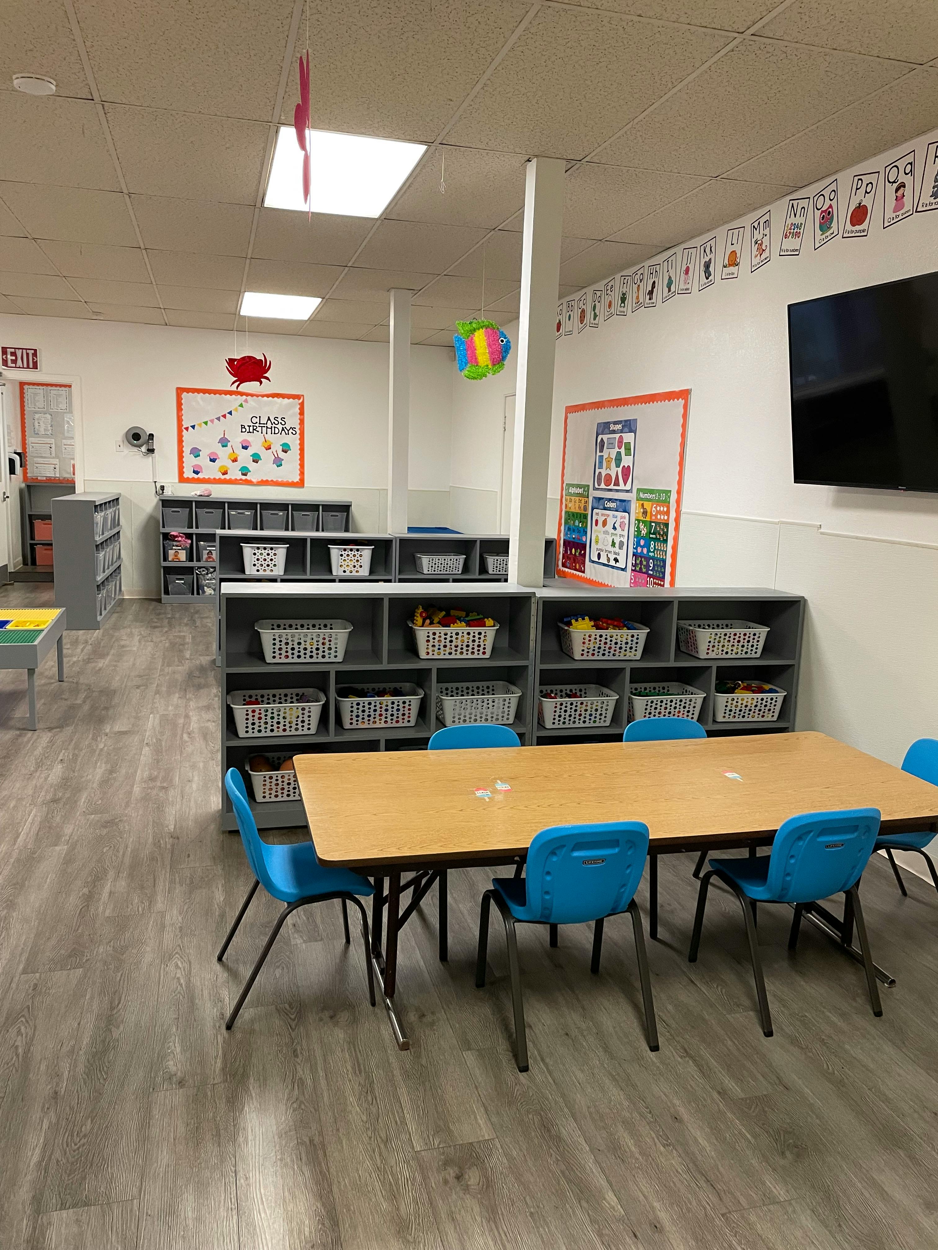 Classroom with tables, blue chairs, and storage shelves with baskets