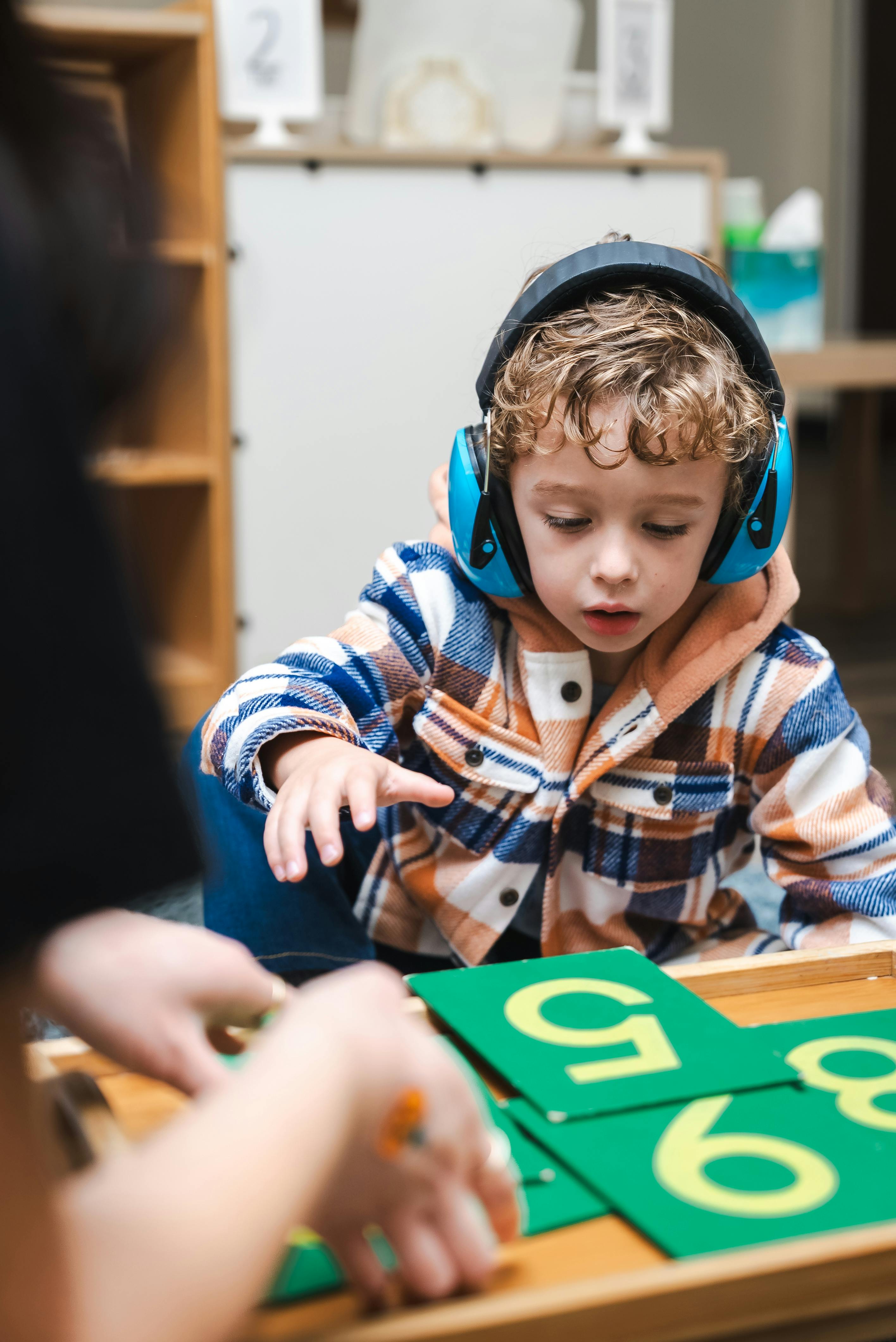 Child wearing headphones reaching for number cards in a classroom