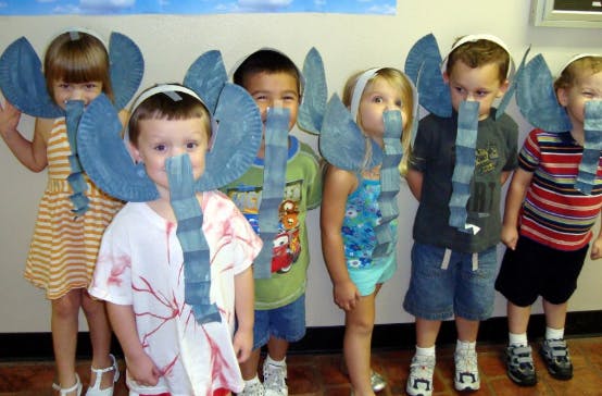 Group of children wearing elephant costumes with paper plate ears and denim trunks