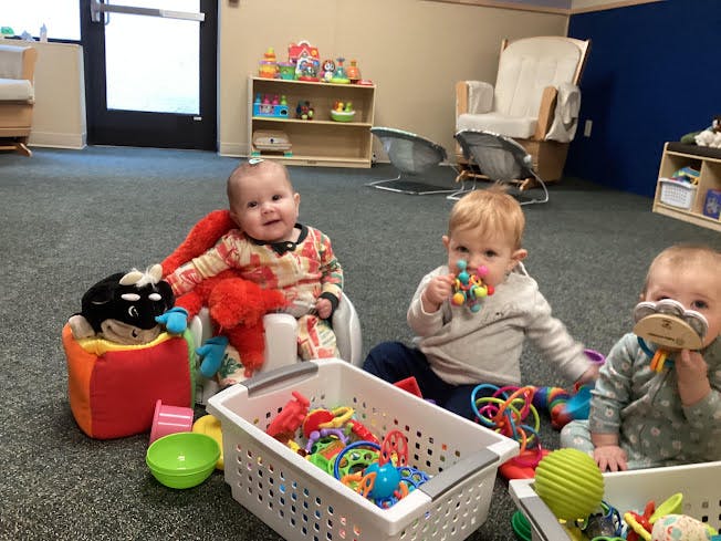 Three babies playing with toys on a carpeted floor