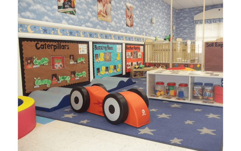 Classroom with children's artwork and an orange toy car on a star-patterned rug