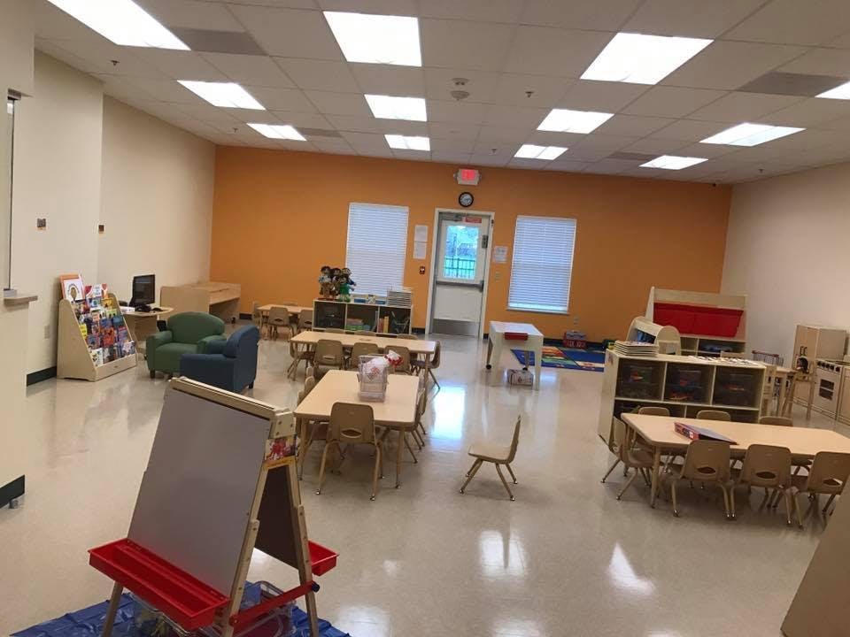 Empty classroom with small tables and chairs, an easel, and a reading nook