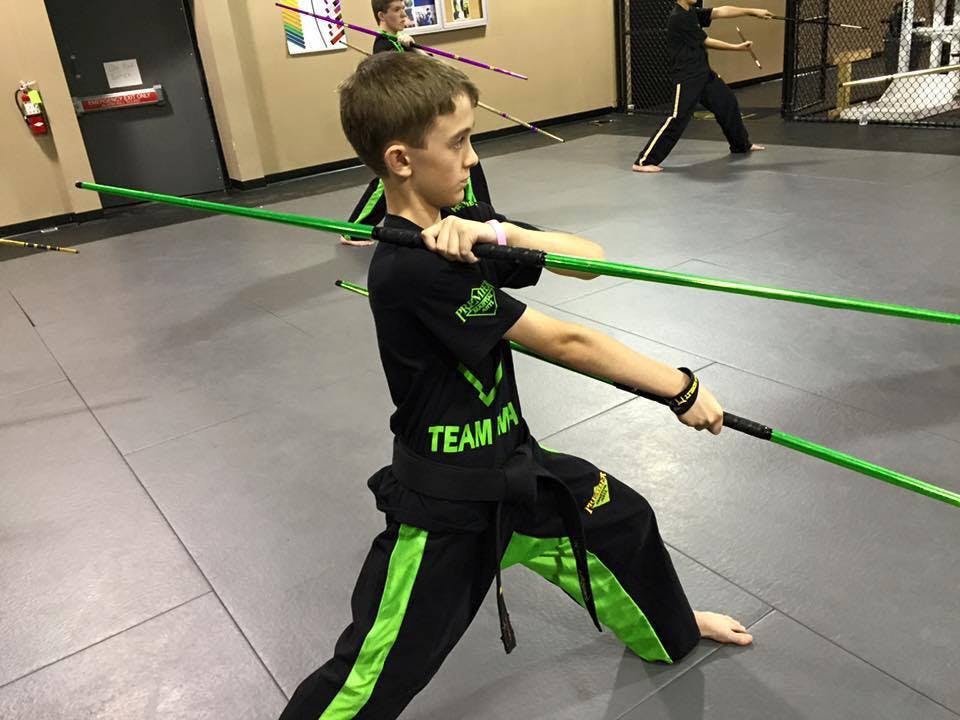 Child in martial arts uniform holding two green staffs