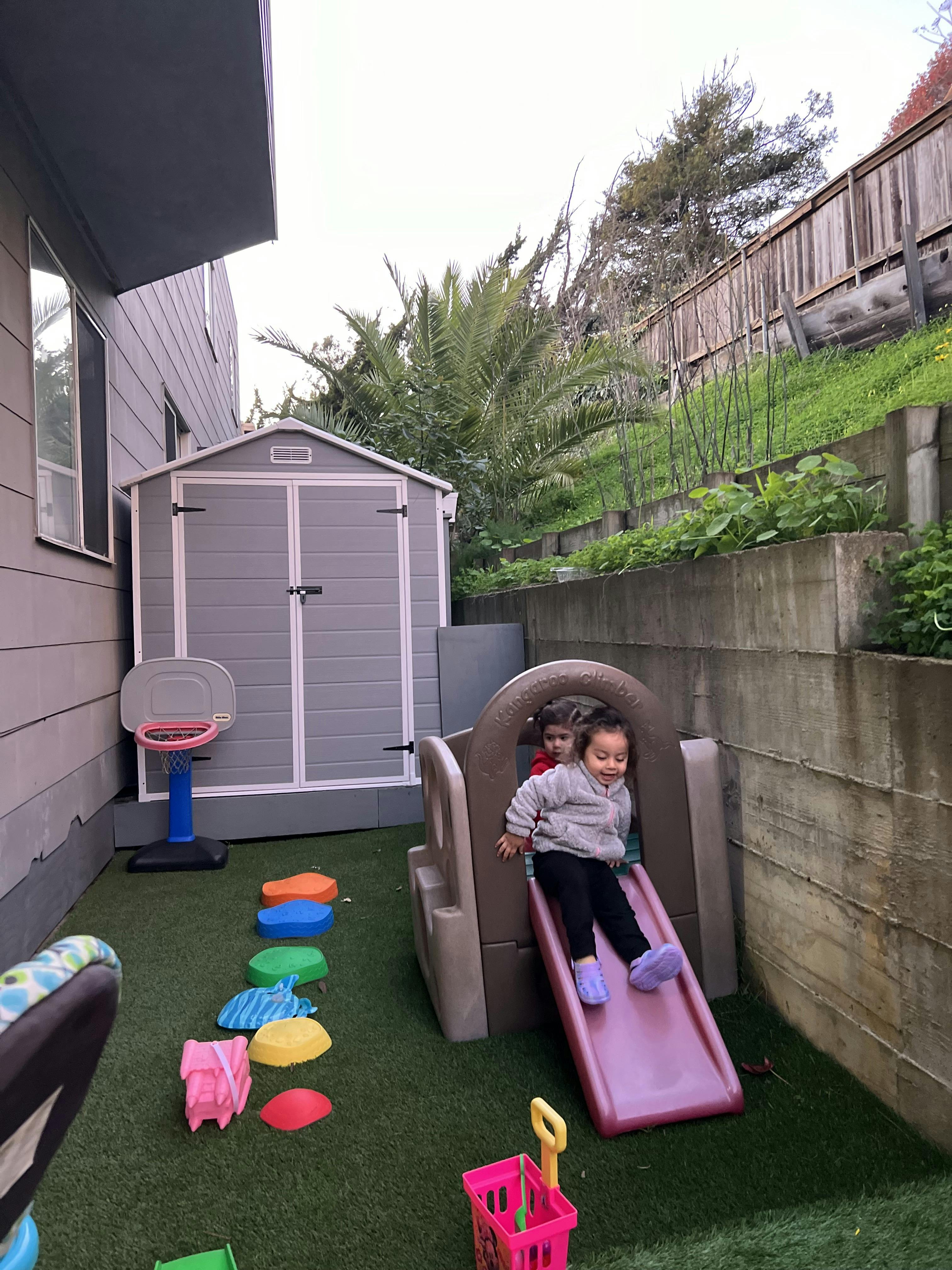 Two children playing on a slide in a backyard
