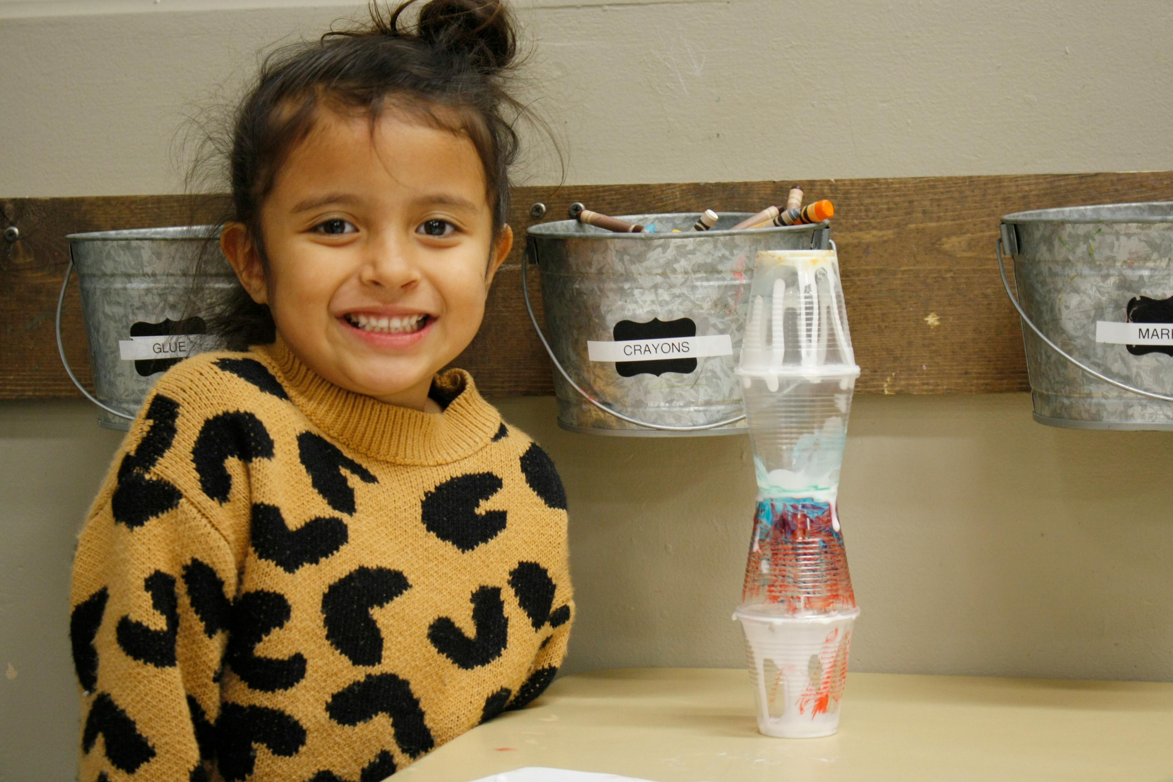 Child smiling next to a stack of plastic cups