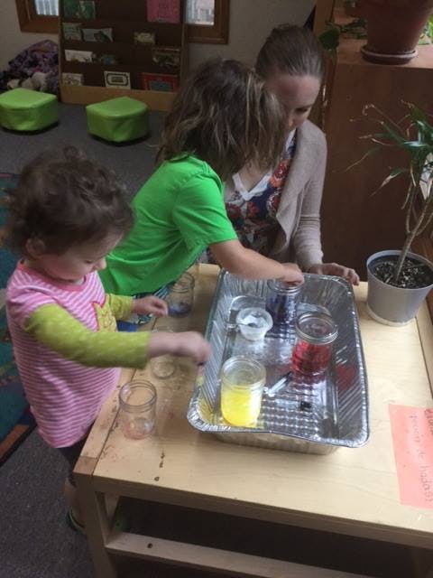 Two children and an adult doing an experiment with colored liquids in jars