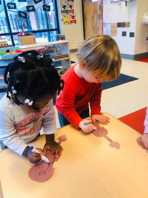 Two children drawing on paper cutouts in a classroom