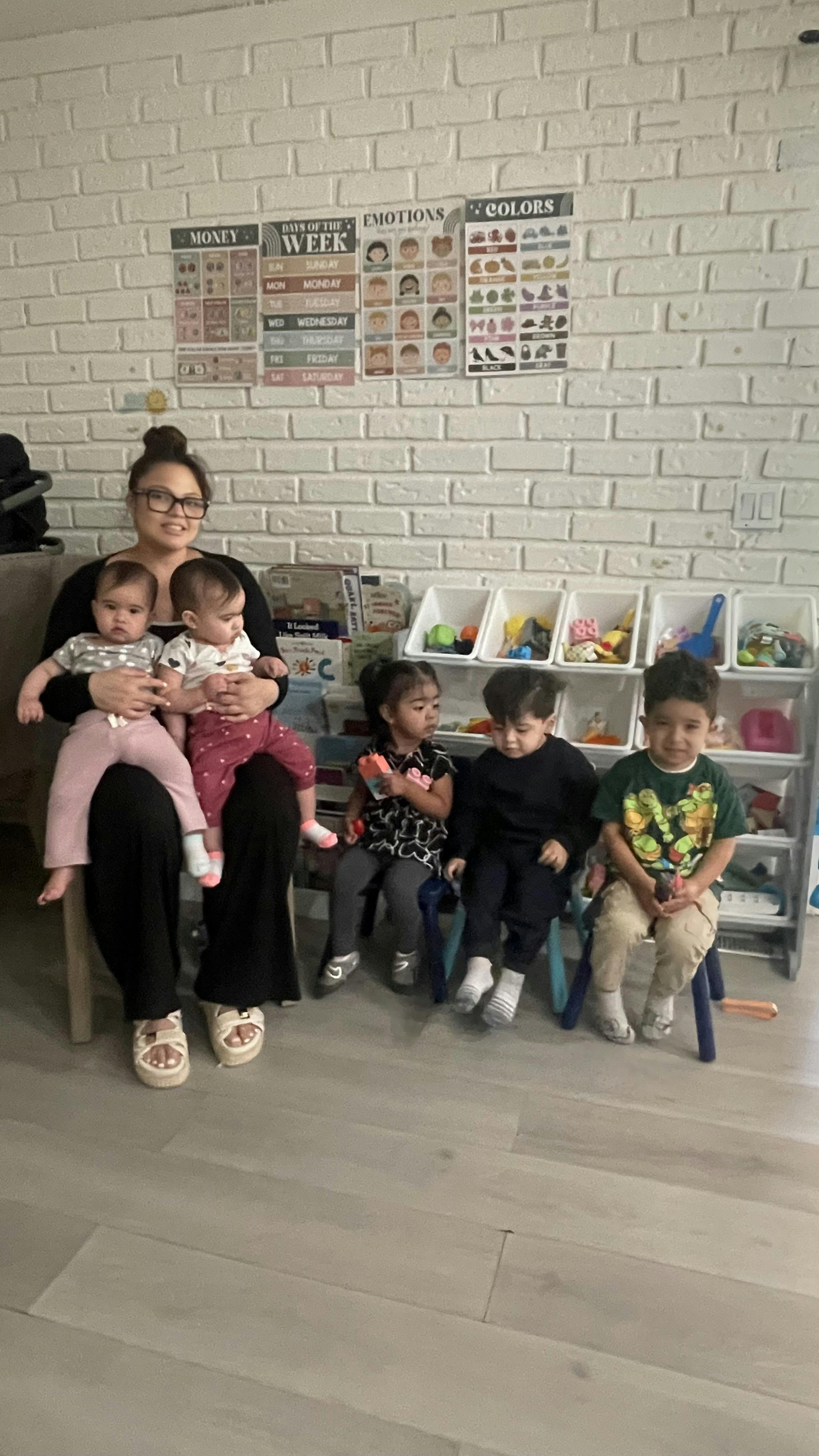Person holding two infants, with three children sitting on chairs beside them