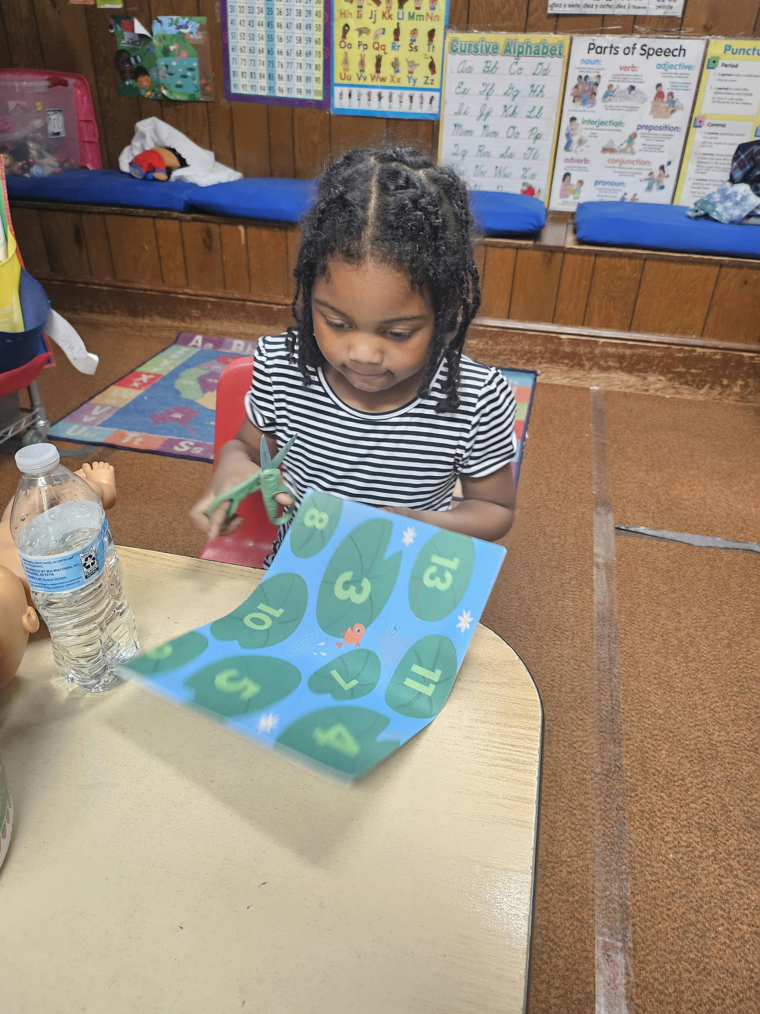 Child using scissors to cut a paper with numbers at a table