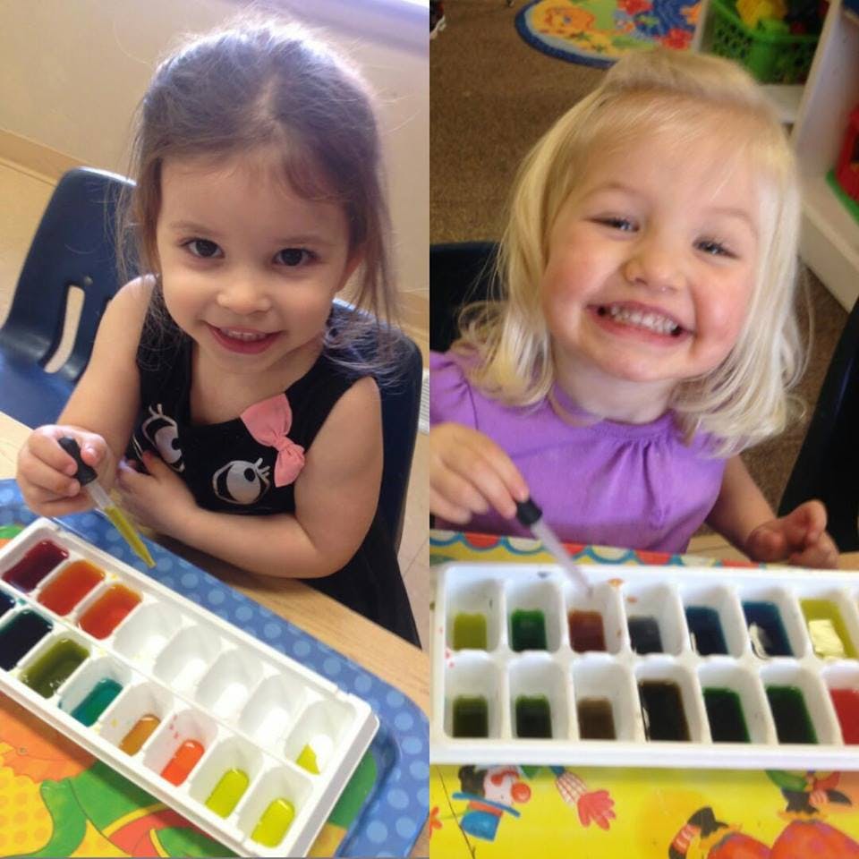 Two children using droppers with colorful liquids in ice cube trays