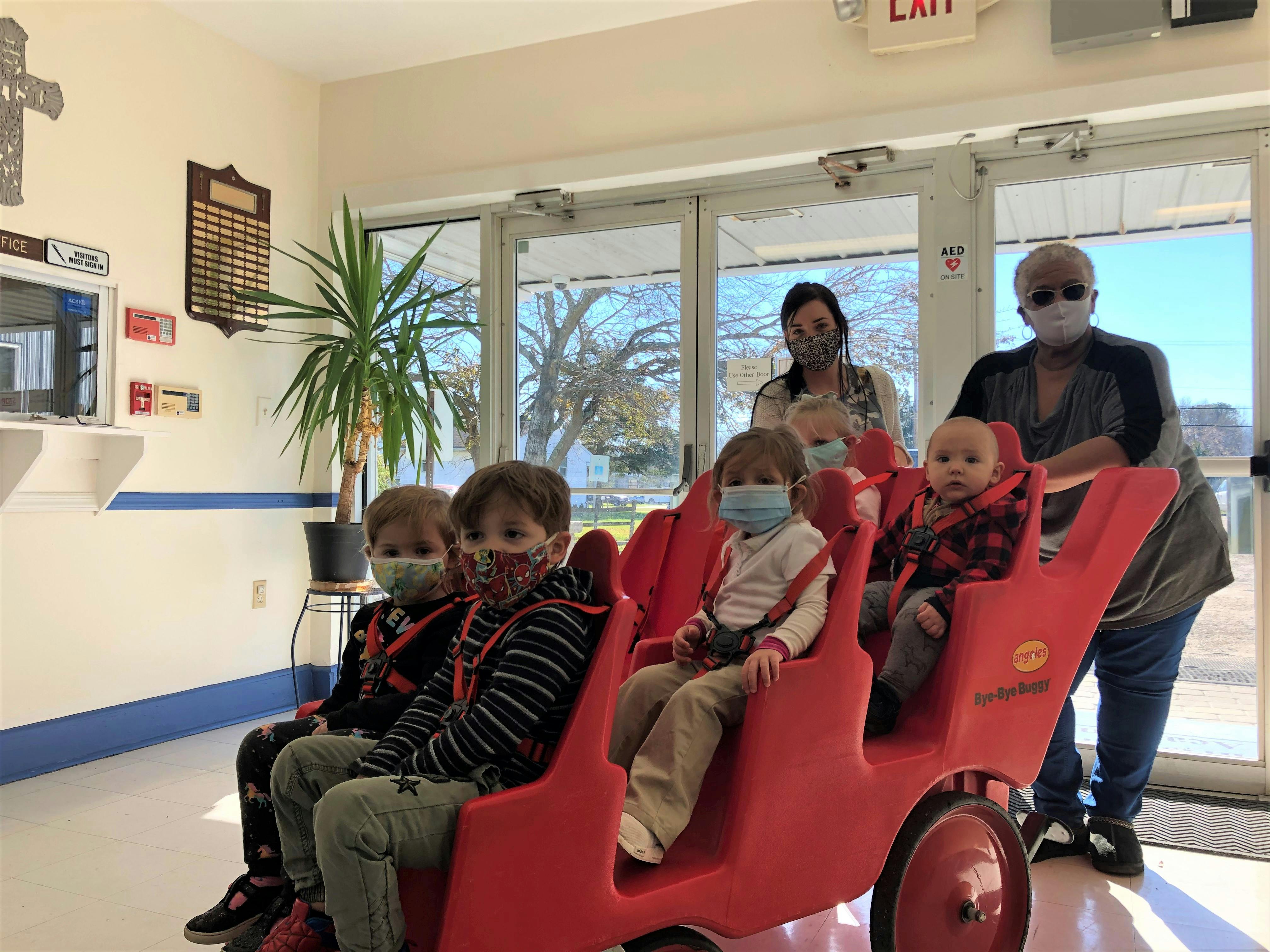 Two adults pushing multiple children in a red multi-seat stroller