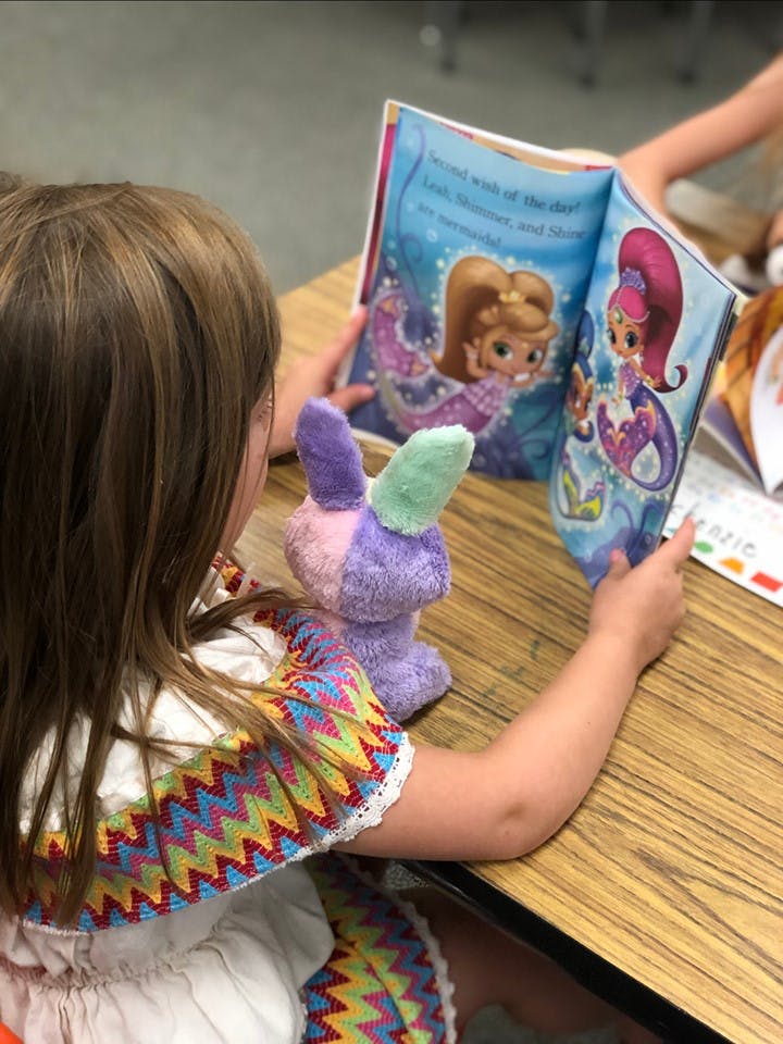 Child reading a book with a stuffed animal on a desk