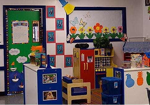 Classroom with a green door, whiteboard with flower decorations, and play kitchen