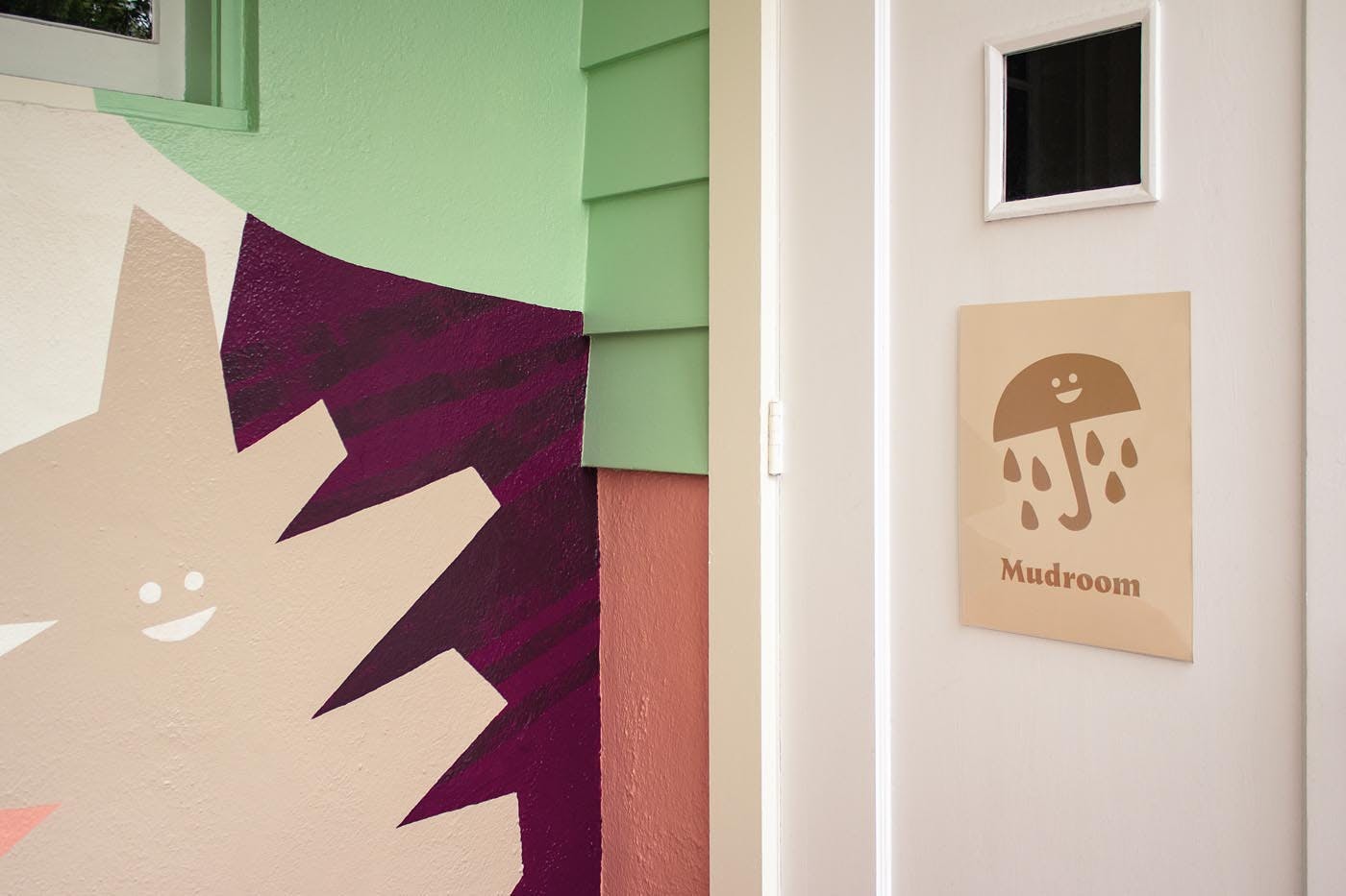 Mural with abstract shapes and a sign with an umbrella icon and the word "Mudroom"