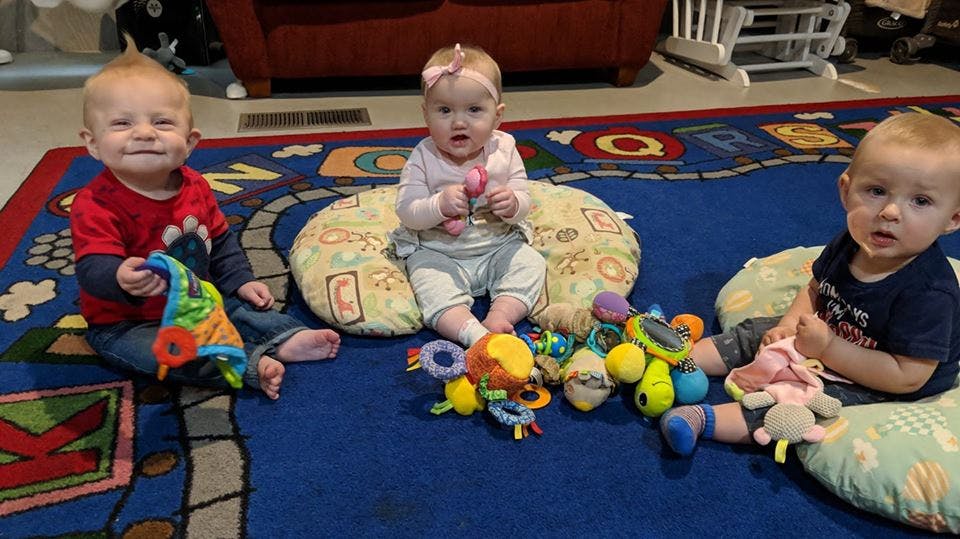 Three babies sitting on a rug with toys