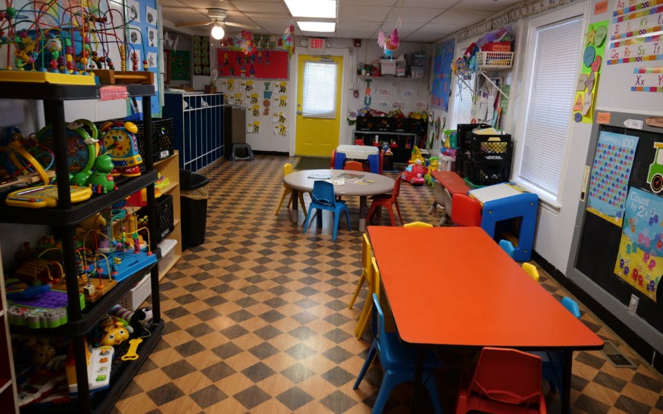 Classroom with small tables and chairs, shelves with toys