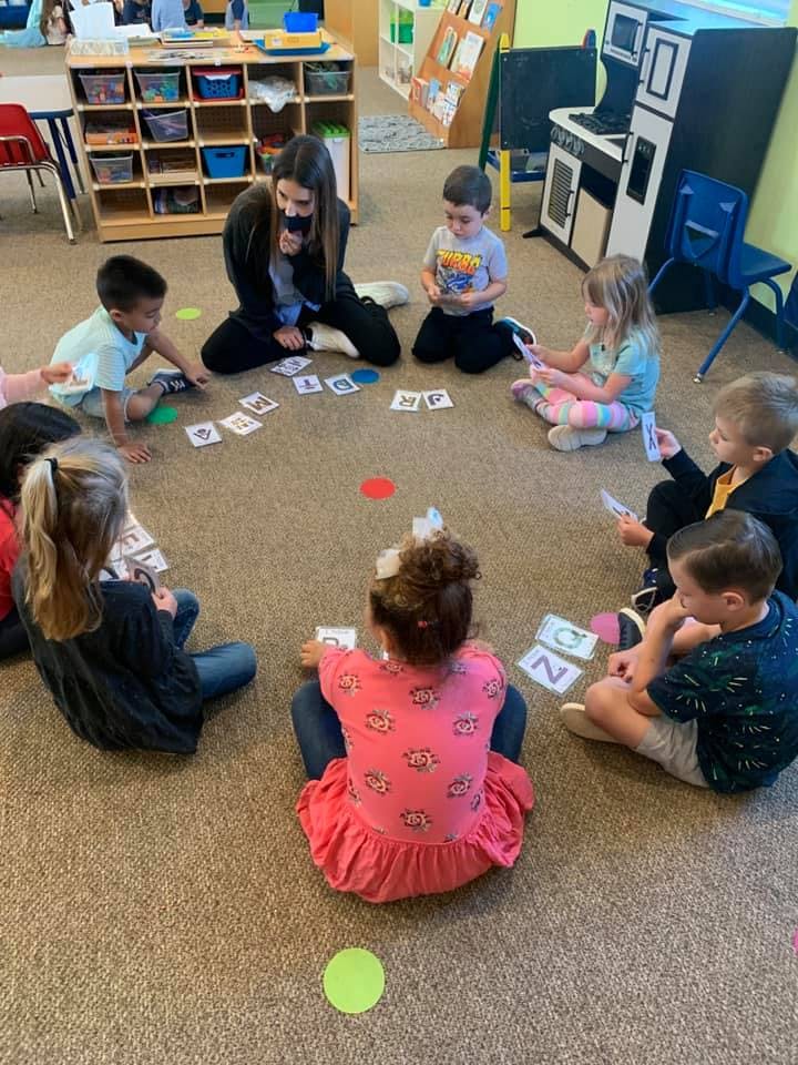 Adult and children sitting on floor in a circle playing with cards