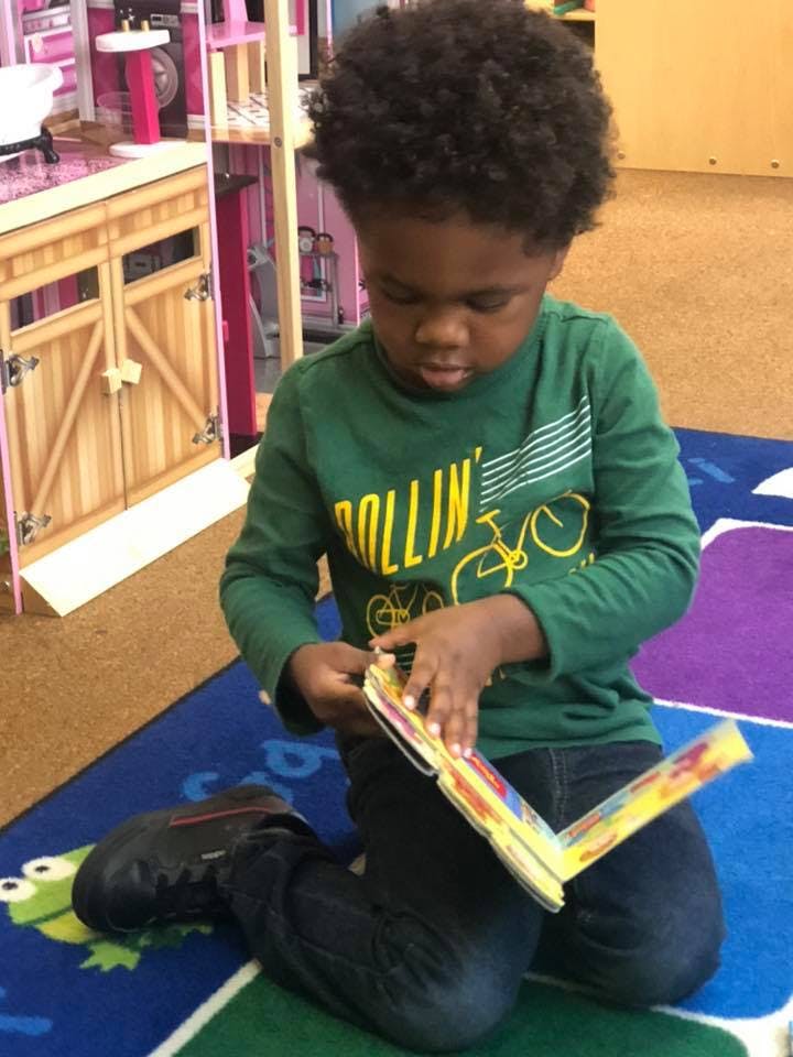 Child kneeling on a rug, looking down at a colorful book